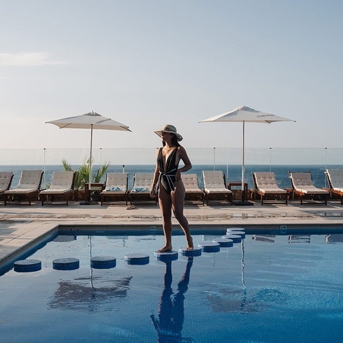 una mujer con traje de baño y sombrero está parada en el borde de una piscina