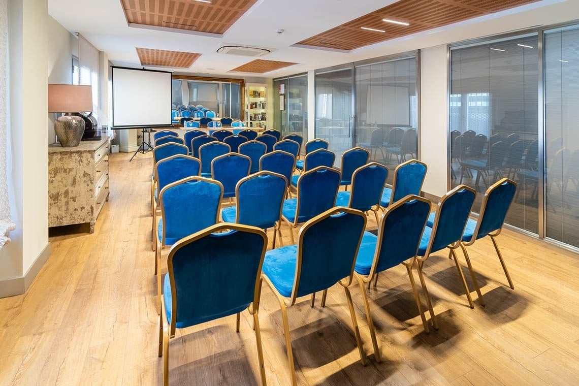 una sala de conferencias llena de sillas azules y una pantalla