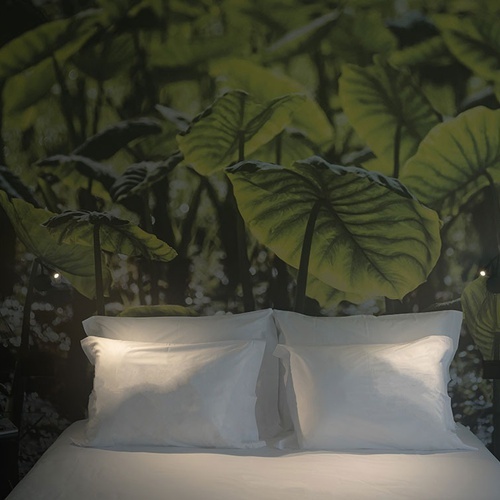 a bed in front of a wall with green leaves on it