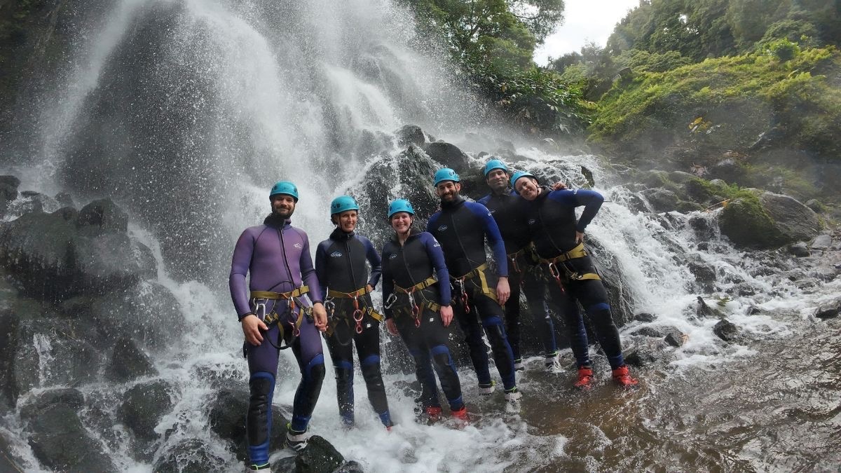 A group of friends by a waterfall after a canyoning activity.