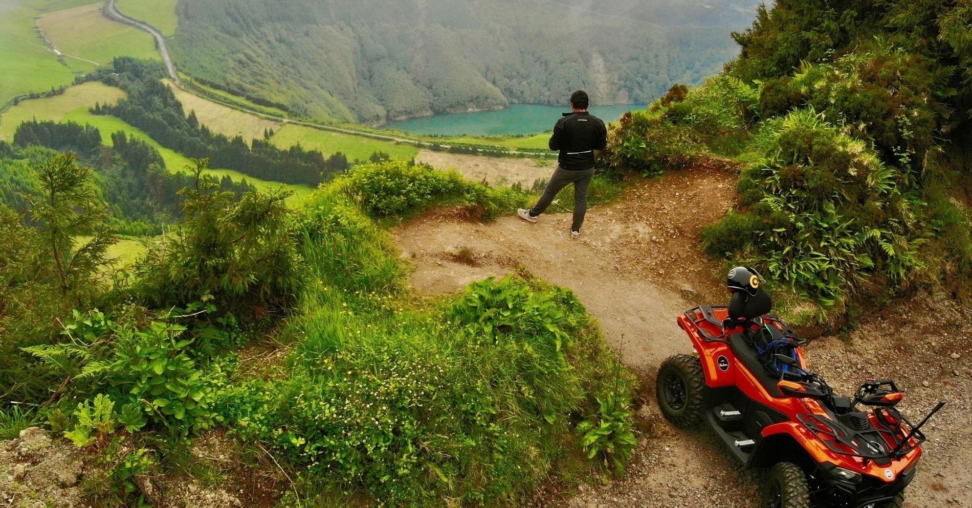 un hombre está parado encima de un atv rojo y mirando un lago