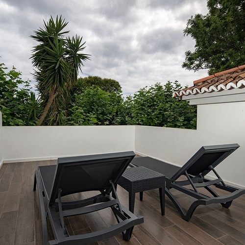 two black lounge chairs sit on a balcony with a palm tree in the background