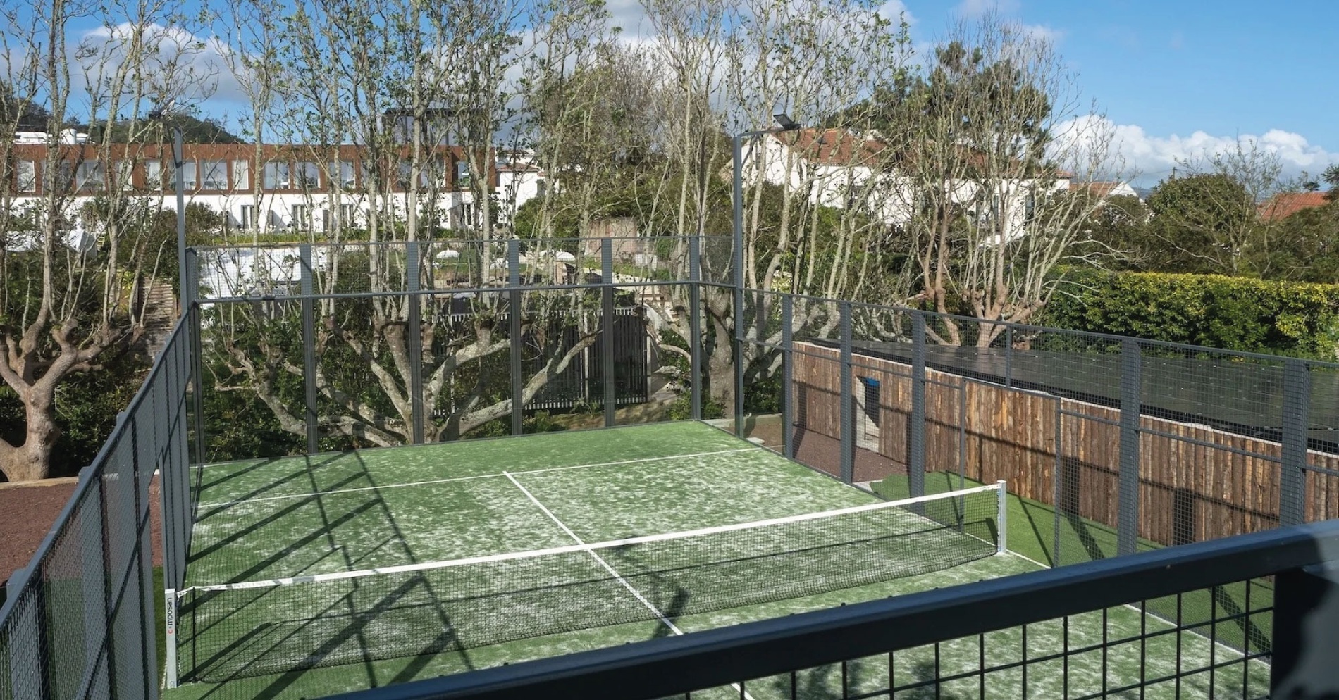 una cancha de tenis está rodeada de árboles y un edificio en el fondo