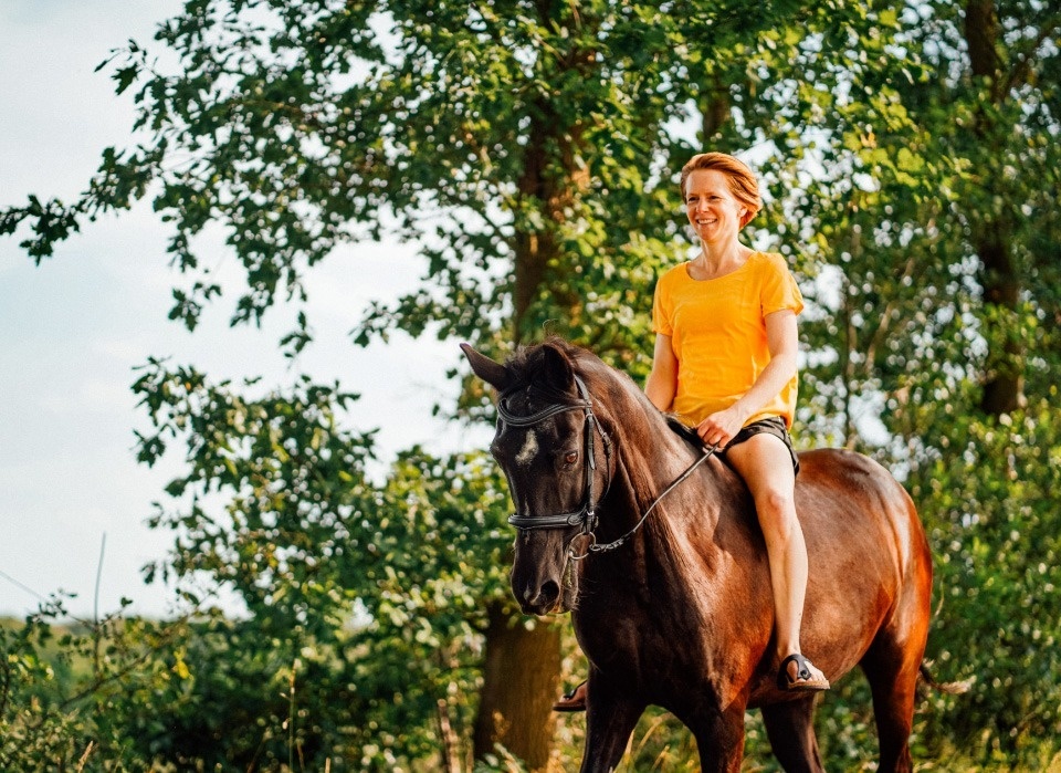 a woman in a yellow shirt is riding a brown horse