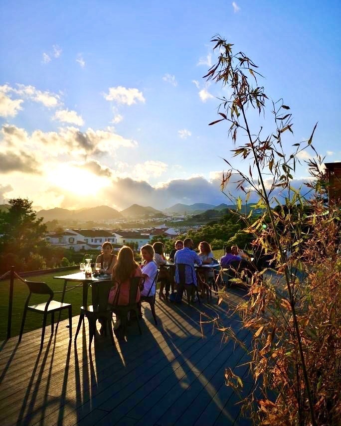 a group of people are sitting at tables on a deck at sunset