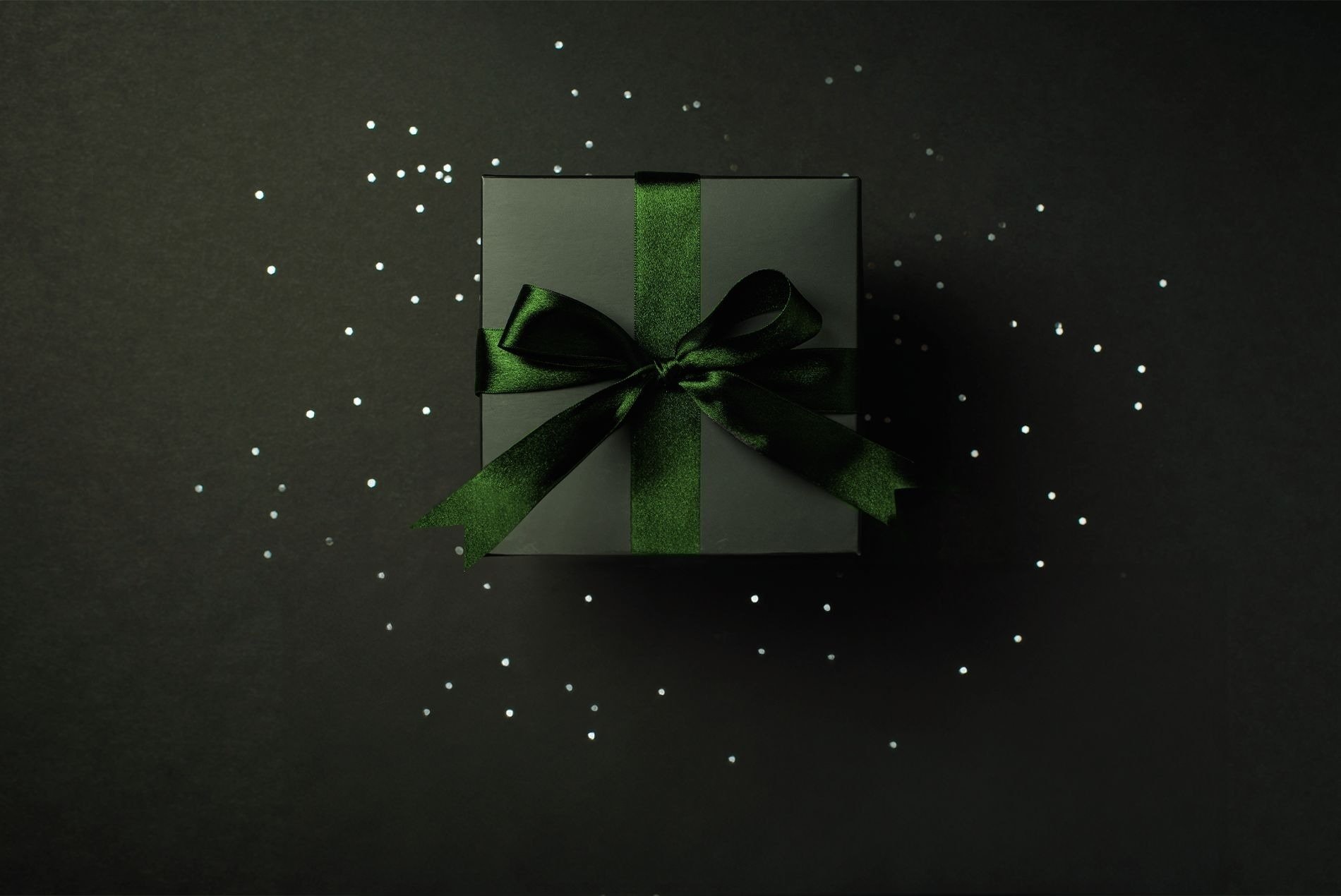 a person is holding a black gift box with a green bow