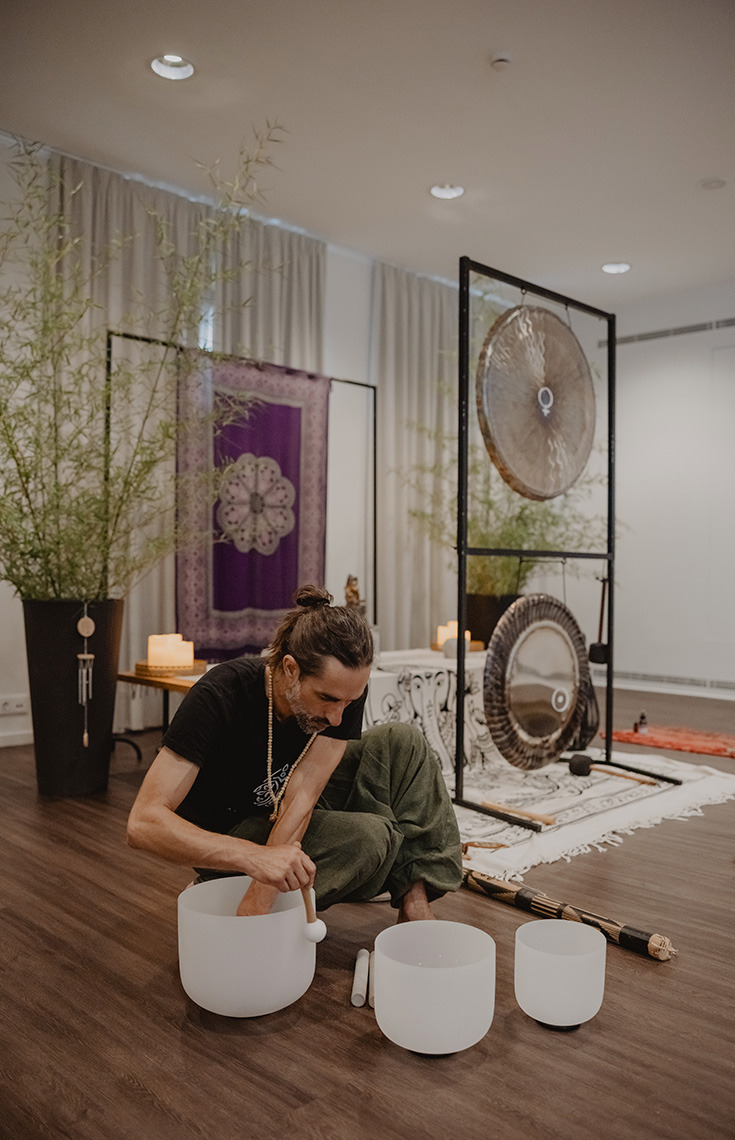 Man playing crystal bowls in a yoga studio with gongs in the background. Senhora da Rosa