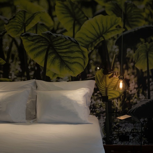 a bed with white sheets and green leaves on the wall behind it