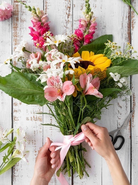 eine Person bindet einen Blumenstrauß mit einem rosa Band