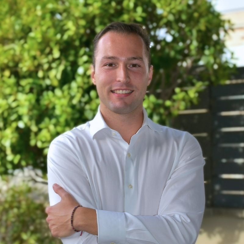  Lächelnder Hotelmitarbeiter in weißem Hemd vor Grün. 