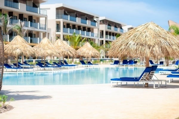 a swimming pool with thatched umbrellas and blue chairs