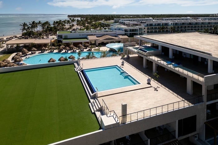 a large swimming pool surrounded by palm trees with the ocean in the background