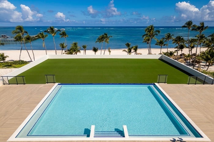 a large swimming pool surrounded by palm trees with the ocean in the background