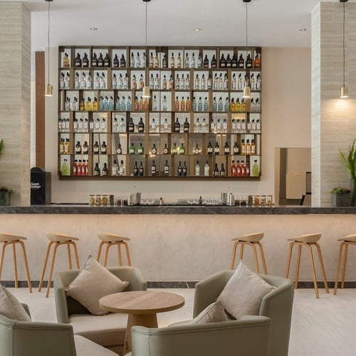 a bar with stools and chairs in front of a wall of liquor bottles