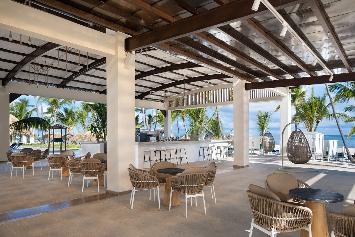 a restaurant with tables and chairs under a canopy with palm trees in the background