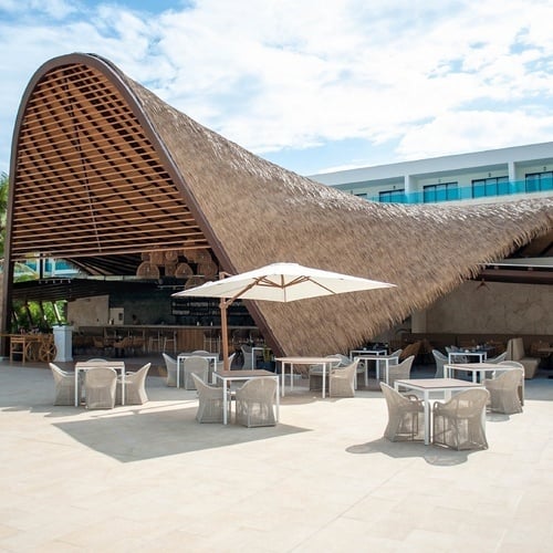 a restaurant with tables and chairs under a thatched roof