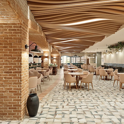 Interior view of a hotel restaurant, featuring brick walls, modern ceiling design, and elegant dining tables. Serenade Caribe Club