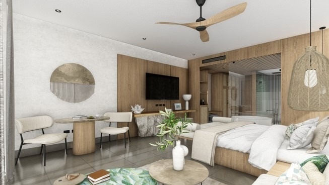 A modern and brightly lit hotel suite features an open-plan bedroom with a wooden bed, a TV area, a small dining nook, and a glass-partitioned bathroom, all decorated with natural wood, white, and light green accents.