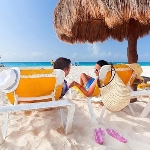 un hombre y una mujer están sentados en sillas de playa bajo un paraguas en la playa .