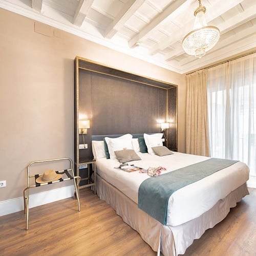 Cómoda habitación de hotel con cama doble, cabecero elegante, lámpara de araña y ambiente moderno.