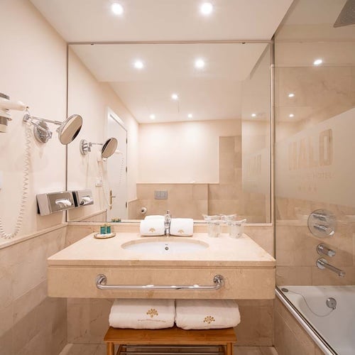 Baño moderno de hotel con lavabo de mármol, gran espejo y ducha/bañera con mampara de cristal.
