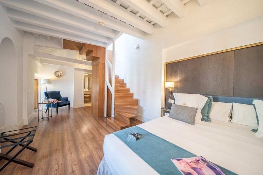 Amplia habitación de hotel con cama, escaleras de madera y zona de estar. SHC: Halo Boutique Hotel