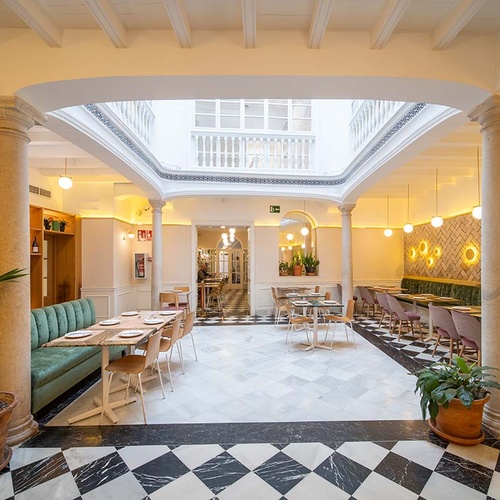 Moderno restaurante de hotel con patio central. Elegante diseño interior, suelo ajedrezado y ambiente luminoso.