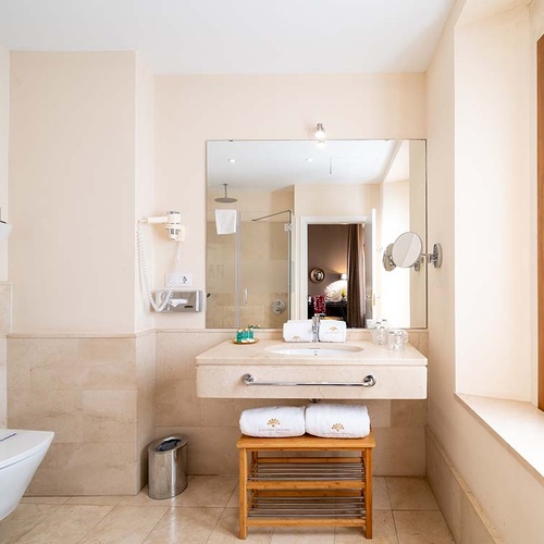 Baño de hotel moderno y luminoso con tocador, espejo grande, inodoro, ducha y secador de pelo.