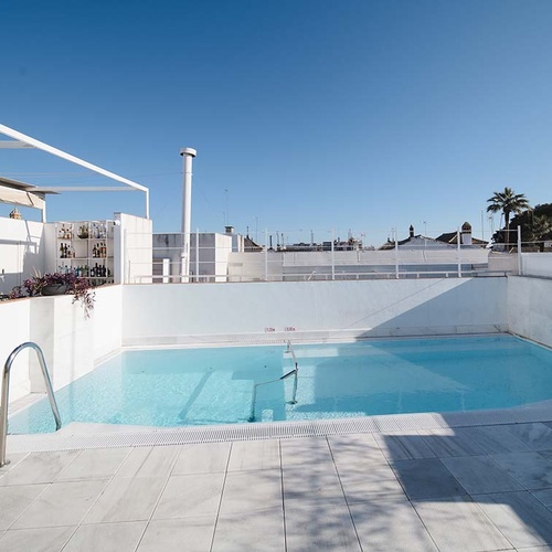 Piscina en la azotea del hotel con bar, vistas a la ciudad y cielo azul claro.