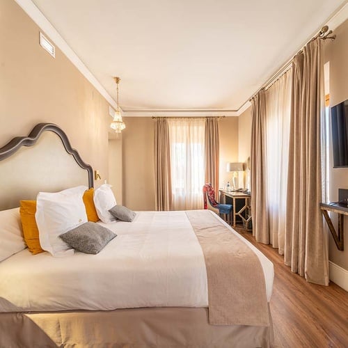 Dormitorio de hotel con cama cómoda, escritorio, TV, cortinas y cabecero decorativo.