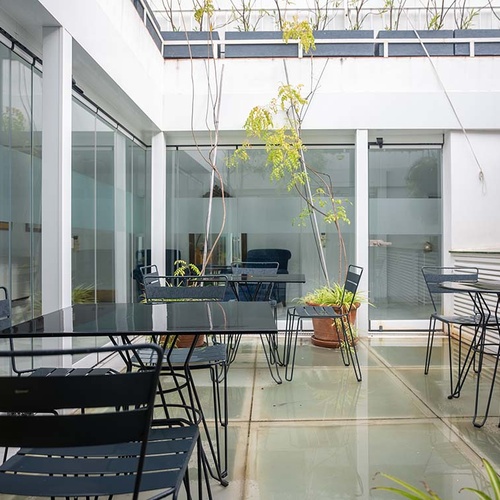 Patio moderno de hotel con mobiliario elegante, paredes de cristal y vegetación, perfecto para un ambiente relajante.