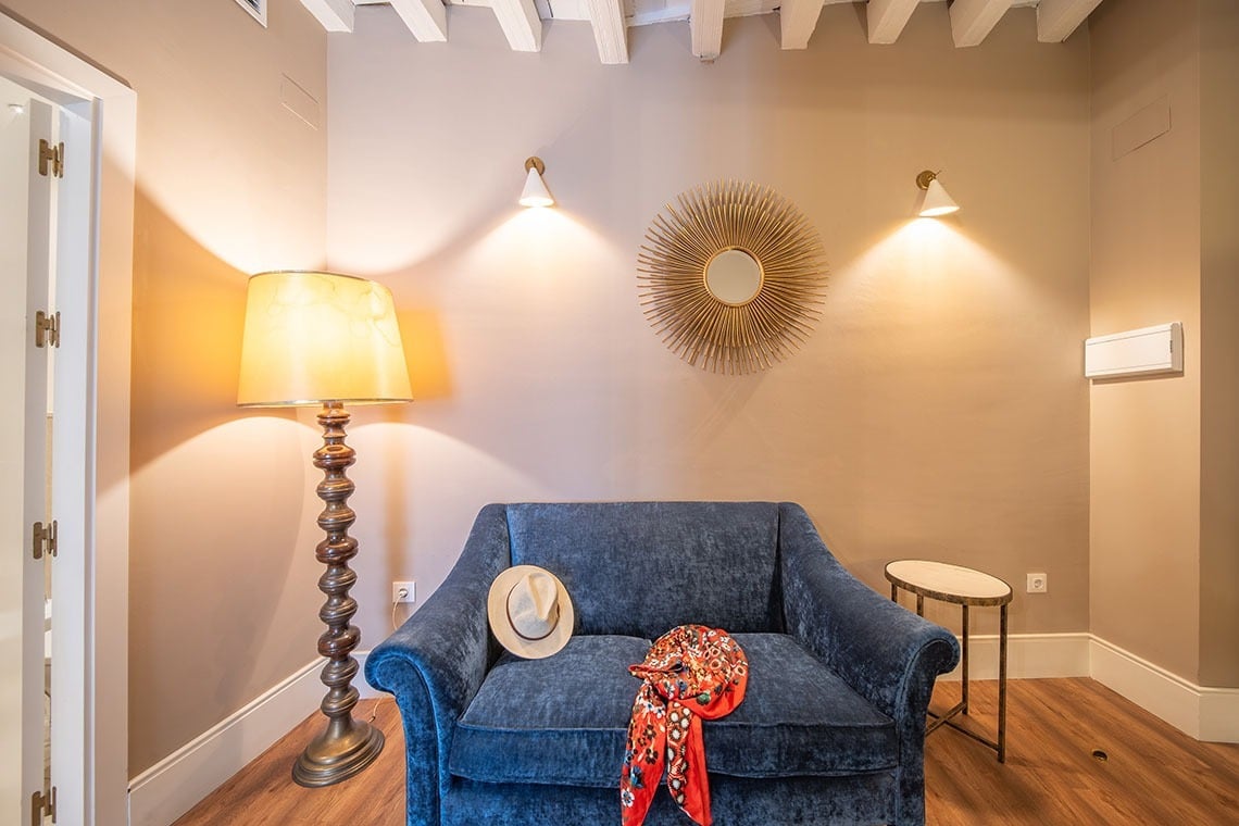 Sofá azul junto a lámpara y espejo sol en habitación de hotel. SHC: Halo Boutique Hotel