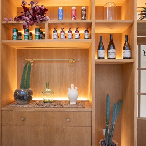 Estantería de madera moderna en hotel, con plantas, botellas y área de baño cercana.