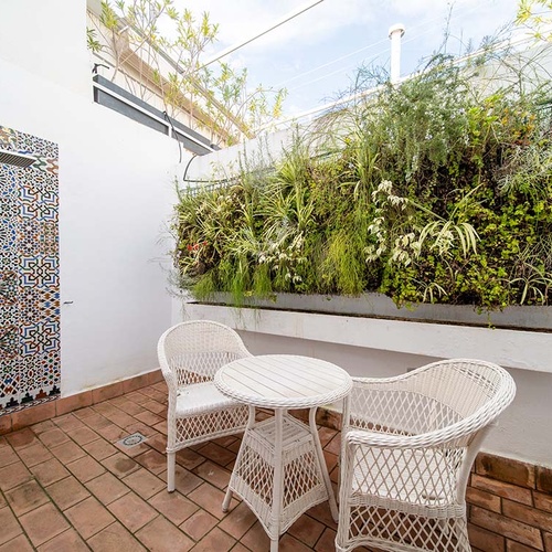 Terraza de hotel con ducha exterior de azulejos marroquíes, jardín vertical y mobiliario blanco para relax.