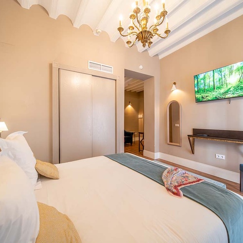 Lujosa habitación de hotel con cama matrimonial, TV, armario y silla de terciopelo azul.