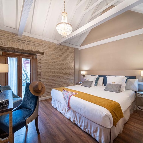 Elegante habitación de hotel con cama king, pared de ladrillo, balcón y decoración rústico-moderna.