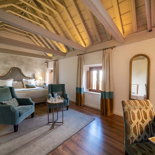 Lujosa suite de hotel con cama king-size, área de estar, escritorio y techo con vigas de madera.