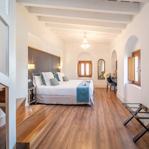 Amplia habitación de hotel con cama grande, decoración elegante, vigas blancas y suelo de madera.