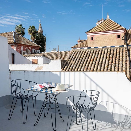 Terraza en la azotea con mesa y sillas, vistas a tejados andaluces y la Giralda de Sevilla.