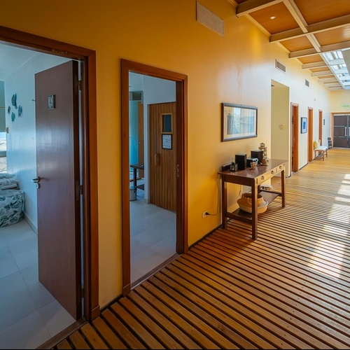 Un corridoio luminoso presenta un pavimento a doghe in legno, pareti gialle e porte che conducono a diversi ambienti, inclusa una stanza con vista sul mare.