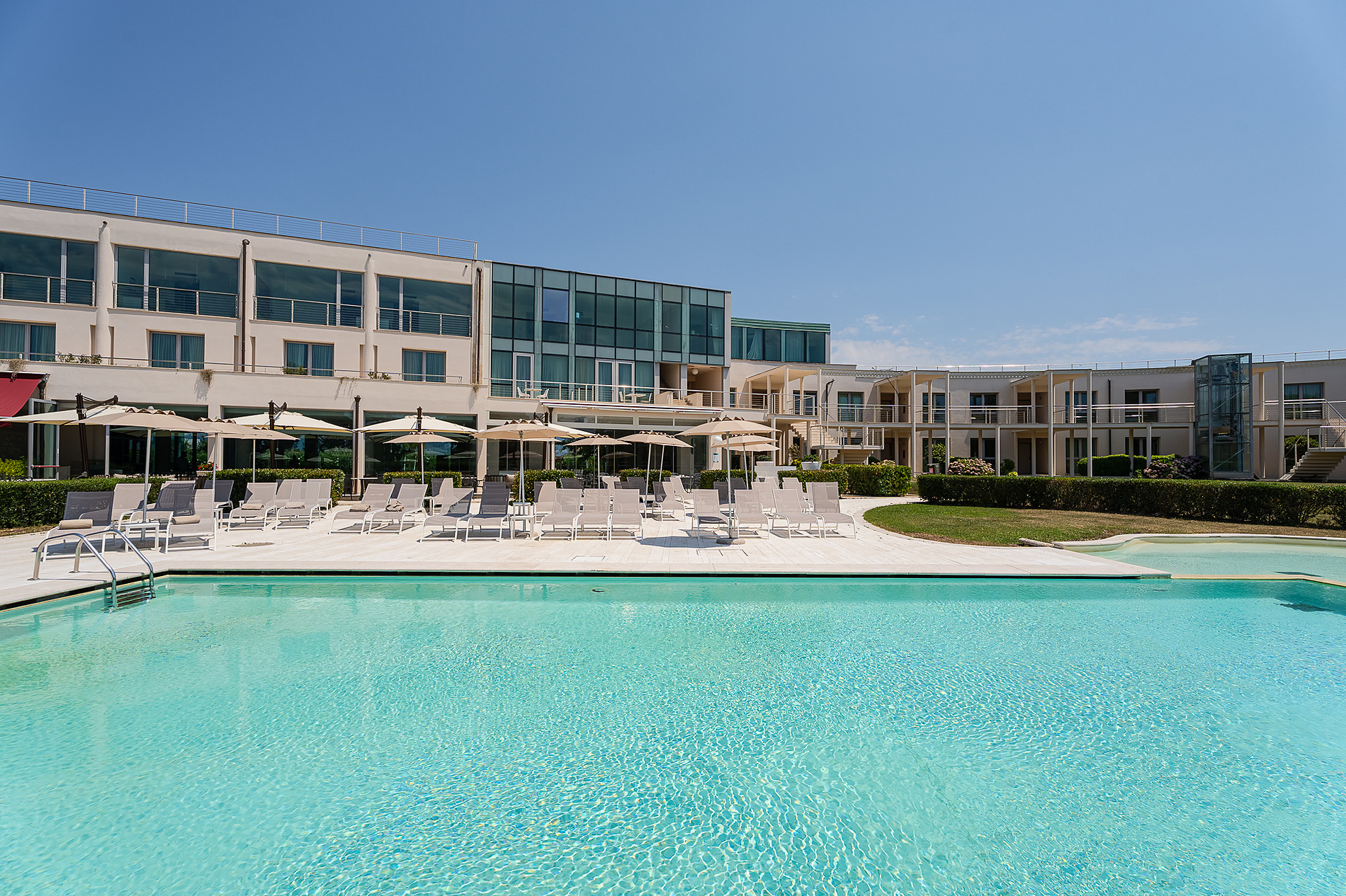 Terrasse d'hôtel avec parasols blancs, chaises colorées et vue sur jardin fleuri. Idéal pour se détendre. Que voir et que faire à Pise | Hôtel Pisa Tower Plaza | Site officiel