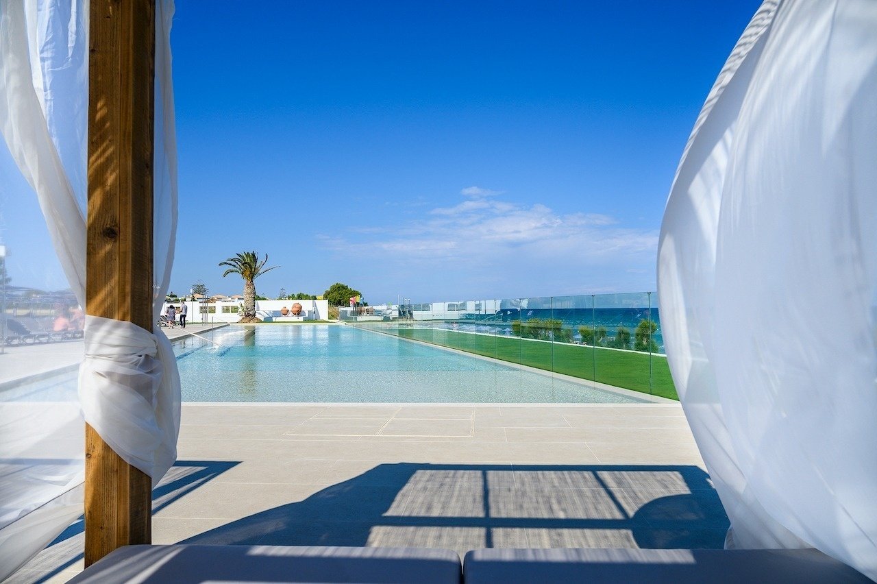 ein weißes Bett mit Blick auf einen Pool und das Meer