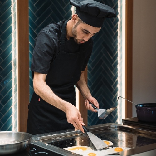 Chef cozinhando ovos na chapa, perfeito para cafés da manhã corporativos Smy.