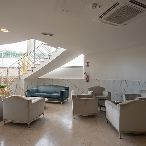 Lobby d'hôtel moderne avec escalier, salons confortables, plantes et décorations dorées. Idéal pour se détendre et se retrouver. Smy: Corporativa.