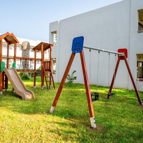 a playground with a slide and swings in front of a white building