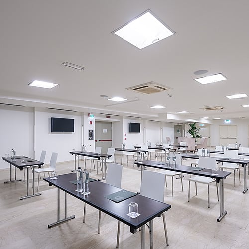 Salle de conférence moderne avec tables et chaises disposées pour une réunion Smy: Corporativa.