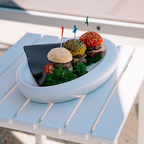 Mini burgers aux couleurs vives et garnitures fraîches, servis sur une table d'hôtel en plein air. Smy: Corporativa