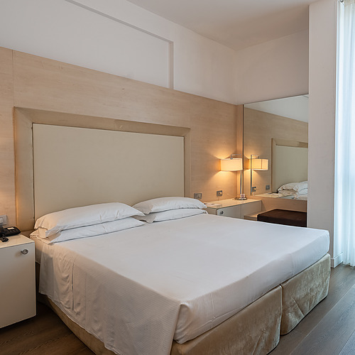 Chambre d'hôtel avec lit, bureau, chaise rouge et lampe. Smy: Corporativa.