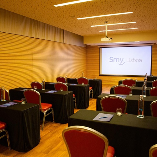 a room with tables and chairs and a screen that says smy lisboa