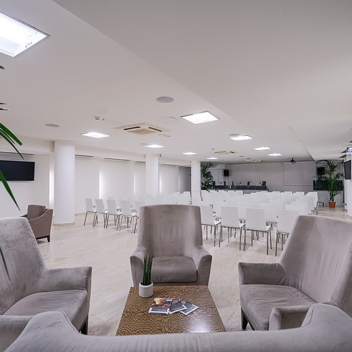Salon d'hôtel spacieux avec chaises, tables basses et projecteur, idéal pour les conférences et événements. Smy: Corporativa